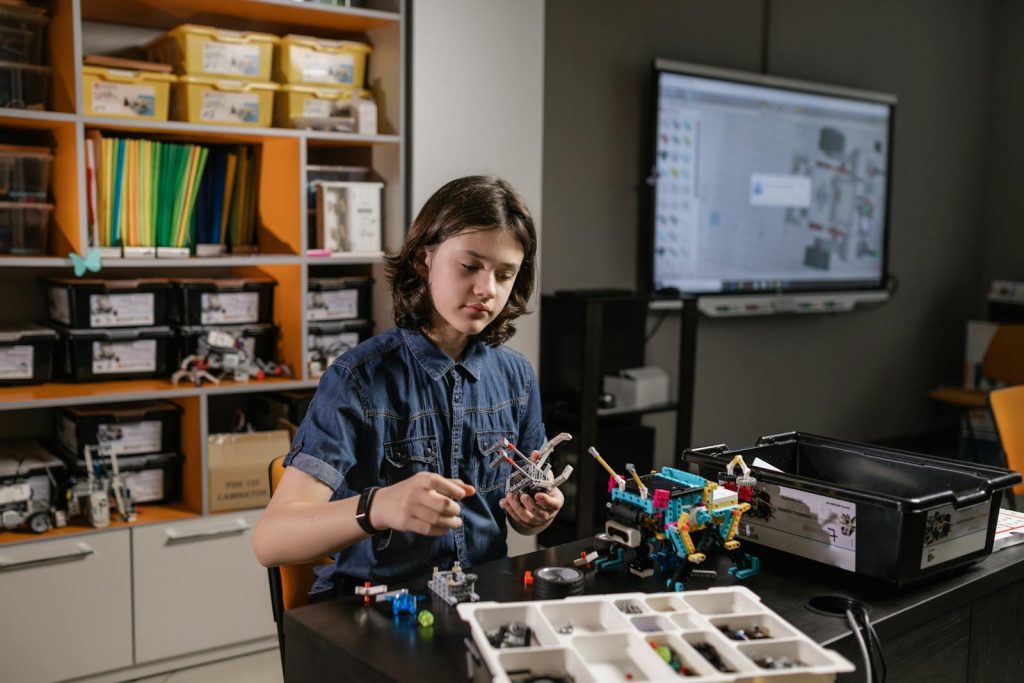 Person in Blue Denim Button Up Shirt Assembling a Lego Robot